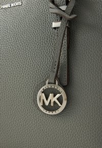Sac en cuir gris à granulés avec pendentif logo MK argenté, fixé par une sangle en cuir, et un détail de couture sur la poignée.
