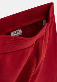 Roter Pullover mit einem gerippten Kragen und weichem Innenfutter. Verfügt über ein Label mit der Aufschrift "GUESS" und subtile Falten am Saum für Textur.
