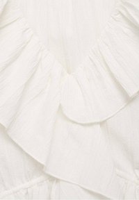Tessuto bianco testurizzato con scollatura a V arricciata e design a strati. Materiale morbido con leggere pieghe e una finitura delicata.