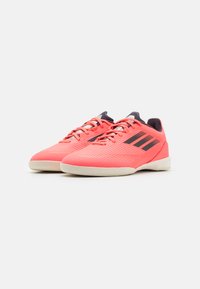 Bright pink athletic shoes with a textured upper, black stripes, and white soles. Features a lace-up design and padded tongue for comfort.