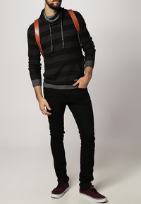 Czarna i szara bluza z kapturem o wzorze w paski, z kołnierzem typu komin, zestawiona z czarnymi jeansami i bordowymi sneakersami. Posiada brązowe paski na ramionach.