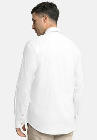 Camisa blanca de manga larga con un ajuste relajado, que presenta un cuello clásico, puños con botones y un dobladillo ligeramente curvado. Textura suave.