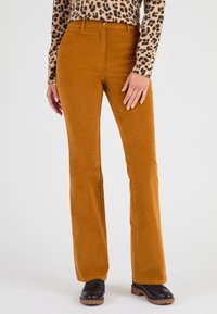Pantalons en velours côtelé couleur moutarde évasés avec une texture lisse, dotés de poches avant et d'une fermeture à bouton. Portés avec un haut à imprimé léopard.