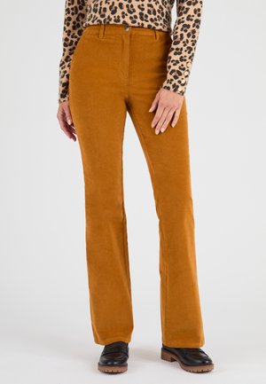 Pantaloni a zampa d'elefante in corduroy color senape con una texture liscia, dotati di tasche frontali e chiusura con bottone. Indossati con un top a stampa leopardata.