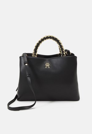 Sac à main en cuir noir avec poignées enveloppées d'une chaîne dorée, bandoulière amovible et petit logo doré au centre avant.