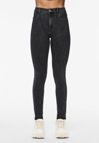 Črne skinny jeans z visokim pasom iz denima, ki imajo klasičen design s petimi žepi in sprednjim gumbom za zapiranje.