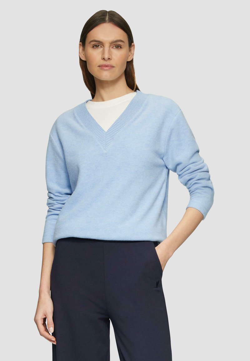 Hellblaues V-Ausschnitt-Pullover aus weichem Material mit geripptem Saum am Kragen und den Bündchen, kombiniert mit dunklen Hosen. Schlichte, lockere Passform.