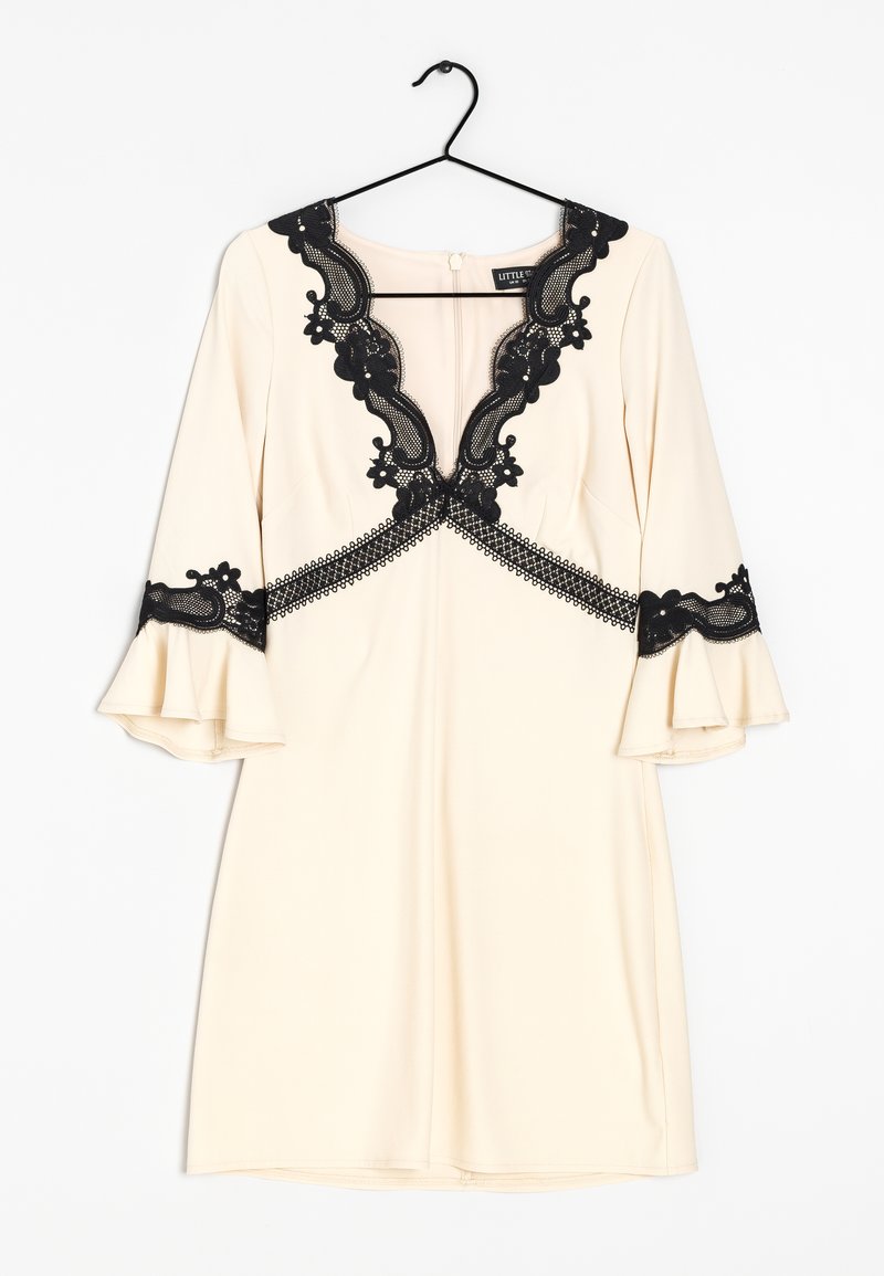 Krämfärgad klänning med svarta spetsdetaljer, V-ringning med blommönster, klockärmar och åtsittande silhuett, hängande på en svart krok.