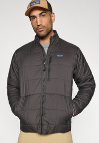 Μαύρο μπουφάν με μόνωση και κεντητό σχέδιο, ψηλό γιακά, φερμουάρ μπροστά και πλαϊνές τσέπες. Συνδυάζεται με γκρι πουκάμισο από μέσα.