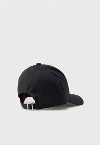 Gorra negra con visera curva, hecha de tela lisa. Cuenta con una correa ajustable con hebilla plateada en la parte trasera y detalles sutiles de costura.