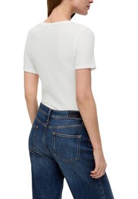 Biała, fakturowana bluzka z krótkim rękawem, zestawiona z wysokim stanem ciemnoniebieskich dżinsów o klasycznym pięcio-kieszeniowym fasonie z kontrastowym przeszyciem.