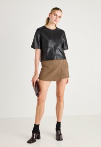 Top curto de couro preto com mangas curtas e decote redondo, combinado com uma saia mini em padrão pied-de-poule. O modelo segura uma mala escura e usa sapatos de salto.