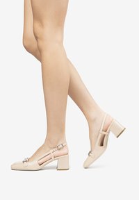 Tacchi slingback beige con punta quadrata, tacco a blocco e dettaglio con fibbia regolabile. Materiale liscio con design a ritaglio per traspirabilità.