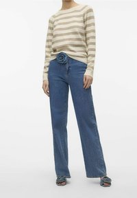 Gestreifter beiger und hellbrauner Pullover mit Rundhalsausschnitt, kombiniert mit hoch taillierten blauen Jeans und blauen Sandalen mit Blumenverzierungen.