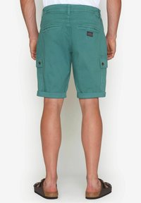 Gröna bomullscargo-shorts med uppvikta fållar, två sidofickor och en bakficka, med en logolapp på midjebandet.