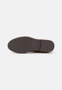 Semelle de chaussure en caoutchouc brun avec un motif texturé et strié. Forme arrondie avec une base plate et un léger talon, présentant une finition soignée.