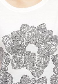 Hvid bomulds T-shirt med et stort sort stregtegning af et blomstermønster med teksturerede kronblade og buede former.