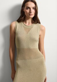 Strickkleid in hellgoldener Farbe mit einer figurbetonten Silhouette, das einen netzähnlichen Bereich an Oberkörper und Taille für zusätzlichen Textur bietet.
