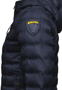 Black puffer jacket featuring a quilted design, a prominent shield logo on the shoulder, and a drawstring at the hem for adjustment.