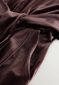 Burgunderfarbener Samtmantel mit Bindegürtel, glatter Textur und drapierendem Design. Der Stoff hat einen sanften Glanz und fließende, plissierte Details.