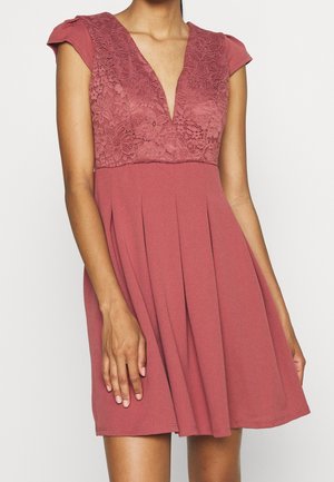 Różowa sukienka z plisowanym dołem, z koronkową górą i krótkimi rękawkami typu cap, zdobiona kwiatowymi wzorami i głębokim dekoltem w kształcie litery V.