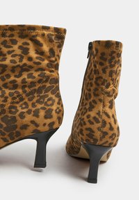 Botines de ante con estampado de leopardo, que cuentan con un tacón de aguja negro y una cremallera lateral. Superficie texturada con un patrón variado.