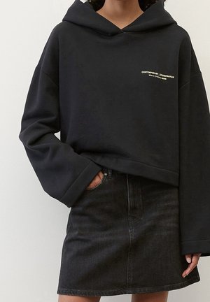 Felpa nera corta con grande cappuccio, caratterizzata da un piccolo logo stampato. Abbinata a una gonna in denim scuro. Tessuto morbido e vestibilità rilassata.