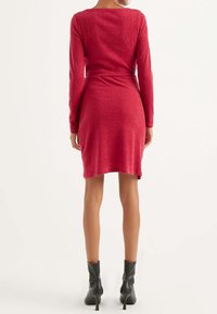 Abito rosso a maniche lunghe in tessuto morbido, silhouette aderente, lunghezza a ginocchio, con scollatura tonda e una leggera arricciatura in vita.