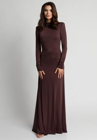 Długa sukienka z długim rękawem w głębokim brązowym kolorze. Posiada marszczenie w talii oraz dopasowane rękawy z delikatnym marszczeniem.