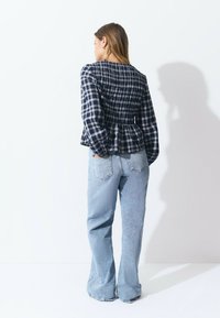 Navy and white checked peplum top with smocking at the waist, paired with light blue flared jeans featuring back pockets.
