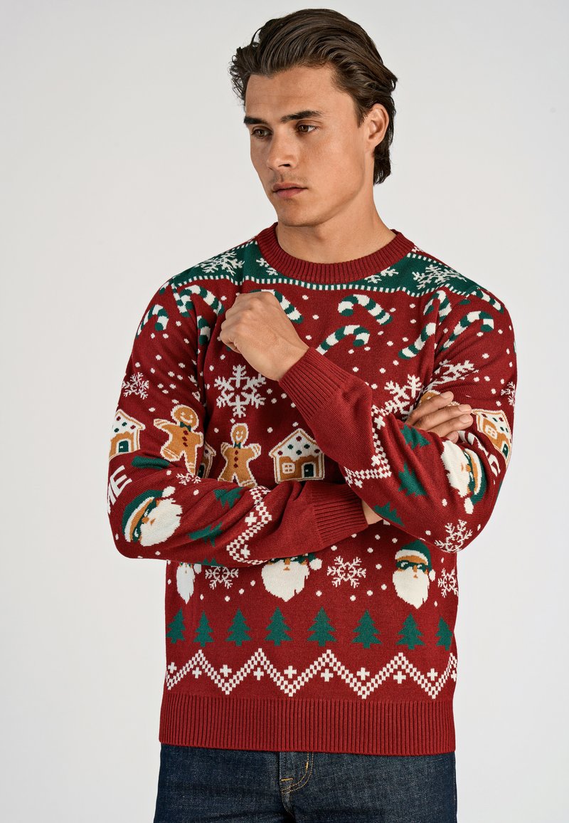 Punainen neulottu joulupaita, jossa on karkkikeppejä, piparkakkuja, lumihiutaleita, puita ja joulupukki-aiheita. Kohokuvioitu kaula-aukko ja hihansuut.