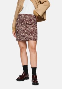 Burgundy mini skirt with a floral pattern, made from textured fabric. Worn with a white top, beige cardigan, black socks, and shiny brown shoes.