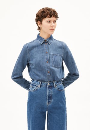Denim overhemd met knopen en kraag, blauwe stof, voorzak en bruine knopen. Gecombineerd met hoog-waist blauwe jeans.