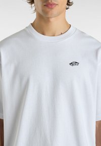 White cotton t-shirt with a crew neck, featuring a small black logo of a skateboard design on the left chest area. Smooth texture.