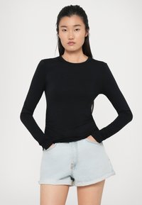 Top aderente nero a maniche lunghe con colletto rotondo, abbinato a pantaloni shorts in denim azzurro chiaro con orlo sfilacciato. Design semplice, texture liscia.