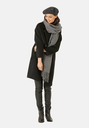 Sort uldfrakke, grå uldsjaal med frynser, sorte læderbukser og en grå beret, hvilket skaber et lagdelt, monokromatisk look.