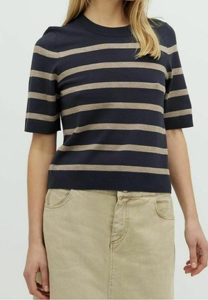 Kobieta nosząca granatowy dziergany top z beżowymi poziomymi paskami i krótkimi rękawami, zestawiony z beżową spódnicą.