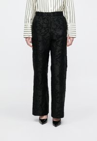 Calças pretas com padrão floral texturizado, design de cintura alta e corte de perna reta. Combinadas com uma camisa de botões às riscas e saltos altos.