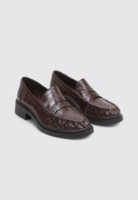 Brown leather loafers with a textured finish, featuring a rounded toe and slight heel. Distinct stitched detailing and pleated edges.