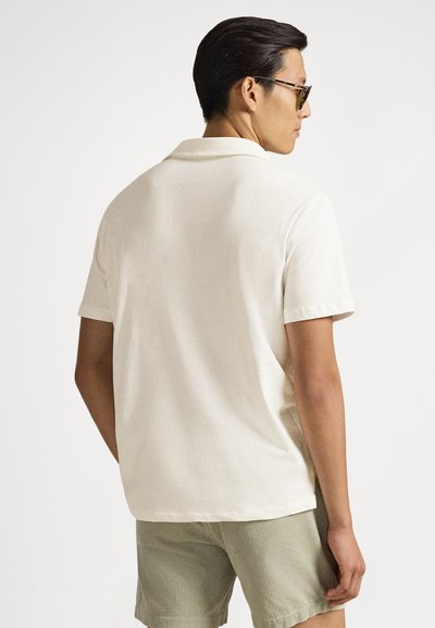 Light cream polo shirt with a soft texture, short sleeves, and a classic collar, paired with green striped shorts.