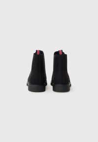 Botines de ante negro con suelas de goma texturizadas, que cuentan con una lengüeta de tirón a rayas de color y un diseño elegante y minimalista.