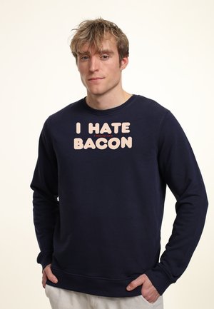 Marineblå sweatshirt med lange ærmer, rund hals, med et lyserødt tekstdesign der siger "JEG HADER BACON" i en rød detalje.