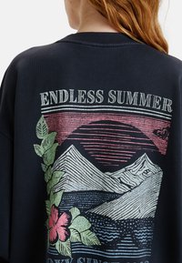 Zwarte sweatshirt met de tekst "ENDLESS SUMMER" en een grafisch ontwerp van bergen en bloemen in roze en groene tinten.