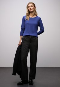 Niebieski, długorękawowy top w połączeniu z ciemnymi, kratowanymi spodniami. Strój cechuje się gładką fakturą i nowoczesnym krojem, uzupełniony czarną kurtką.