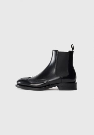 Stivaletti Chelsea in pelle nera con dettagli brogue, finitura liscia, pannelli laterali elastici e tacco a blocco basso. Design resistente e di stile.