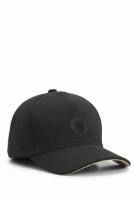 Schwarze Baseballmütze mit runder Krone, die auf der Vorderseite ein schwarzes Logopatch und einen kontrastierenden goldenen Akzent am Schirm hat.
