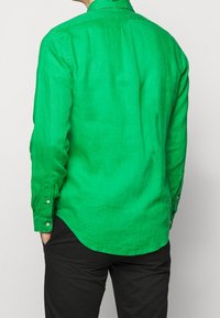 Grön linne skjorta med långa ärmar, rak nederkant och knäppta manschetter, som visar en texturerad yta och svag lyster.