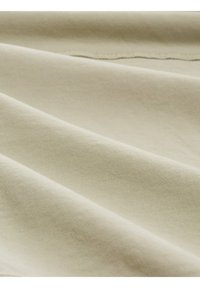 Beige Stoff mit glatter Textur, der subtile Falten und ein feines Webmuster zeigt, wodurch das natürliche Licht seinen sanften Glanz betont.