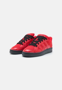 Røde sneakers med en blanklakkert finish, svarte snørebånd, en teksturert mesh-tunge og en svart gummisåle med tre sidestreker.