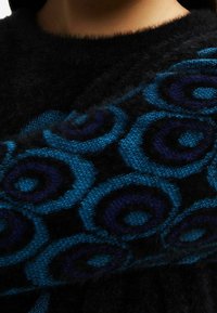 Svart ulltröja med en strukturerad design och blå och lila cirkulära mönster som ger en kontrasterande och livfull visuell detalj.